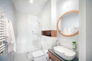 A modern bathroom with a glass-enclosed shower, a white toilet, a wooden vanity, and a round mirror. - Suntago Village (Mszczonow)