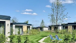 A row of modern, single-story buildings with a well-maintained lawn and a few trees. - Suntago Village (Mszczonow)