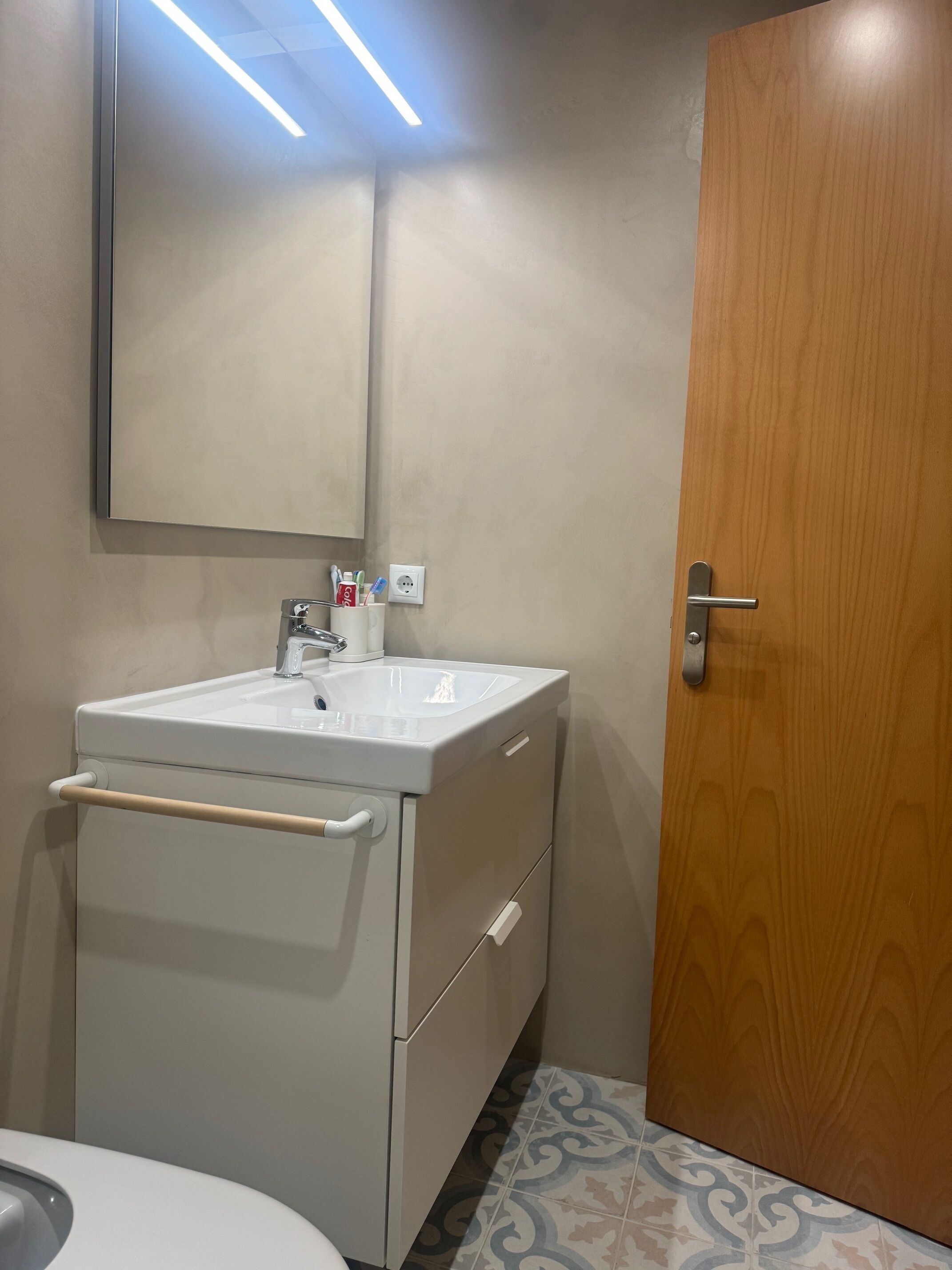 Ett badrum med ett vitt handfat, en spegel och en dörr av trä.