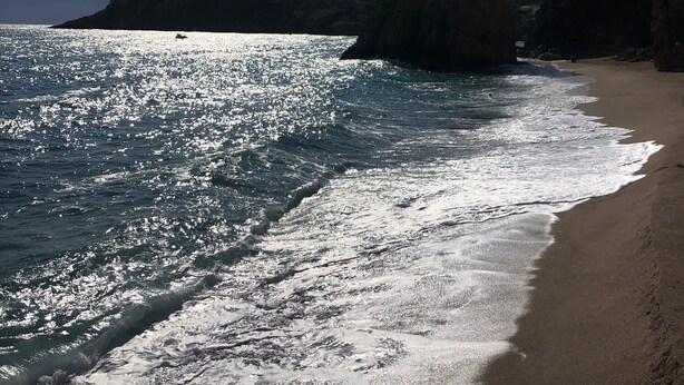 Ein Strand mit klarem Wasser, sandigem Ufer und felsigen Klippen unter einem strahlend blauen Himmel.