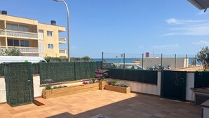Eine Terrasse mit Tisch und Stühlen, ein grüner Heckenstreifen und Meerblick.