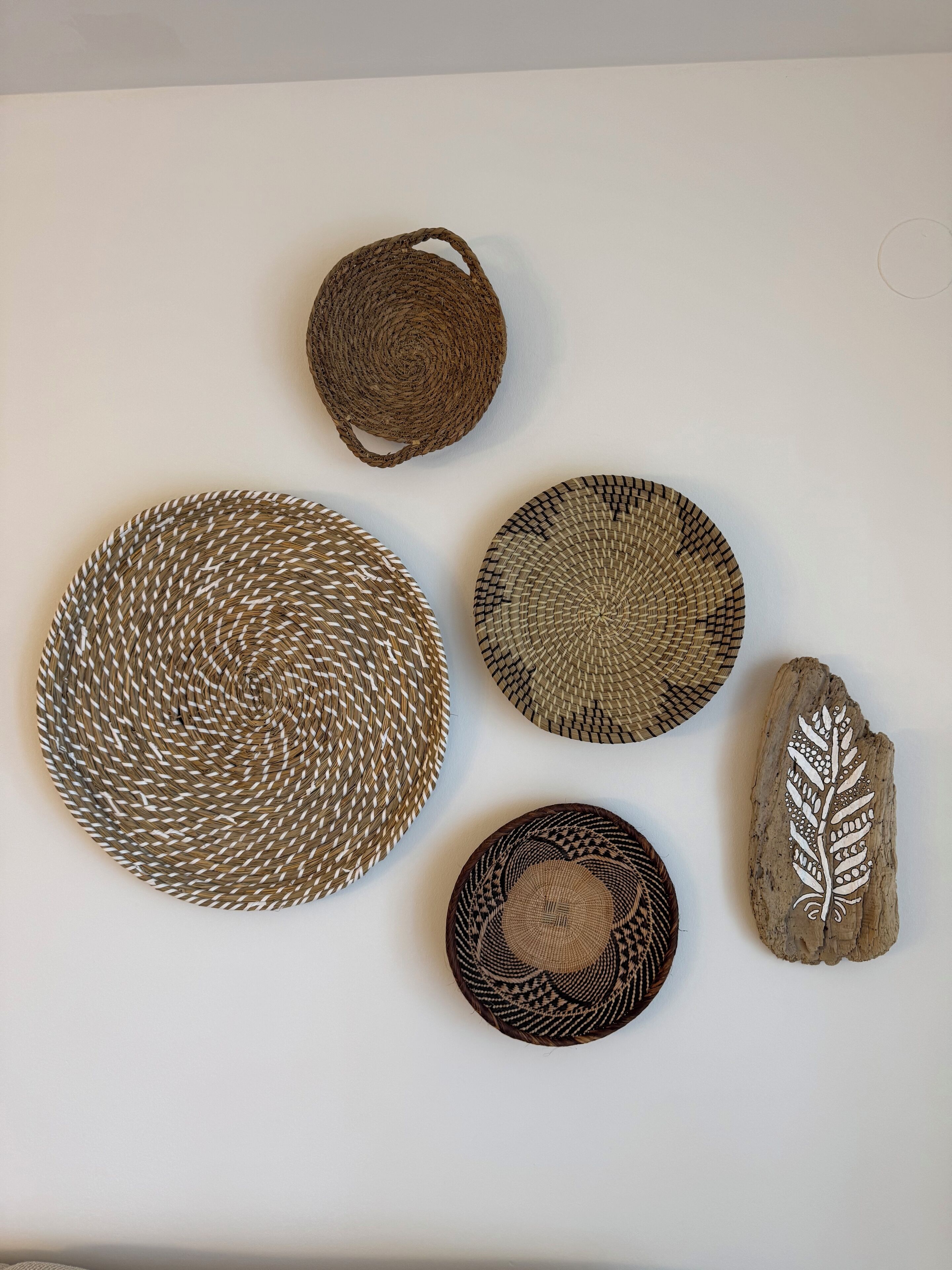 A collection of woven baskets and a carved wooden piece on a plain wall.
