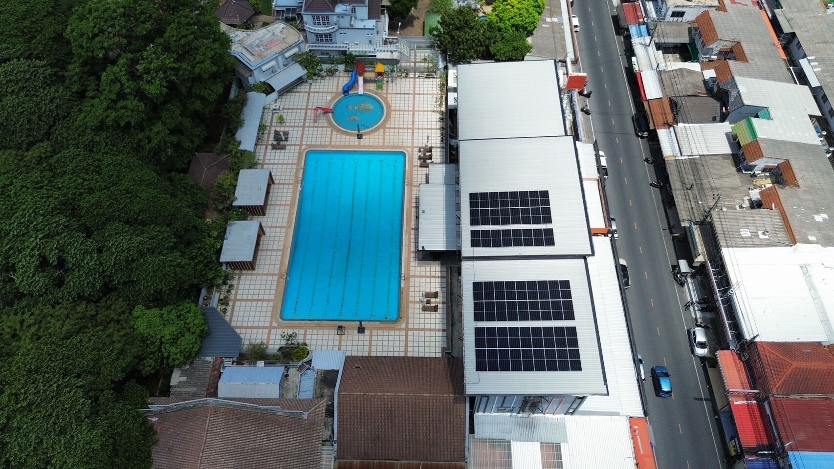 An aerial view of a building with a swimming pool, solar panels, and a road adjacent to it.