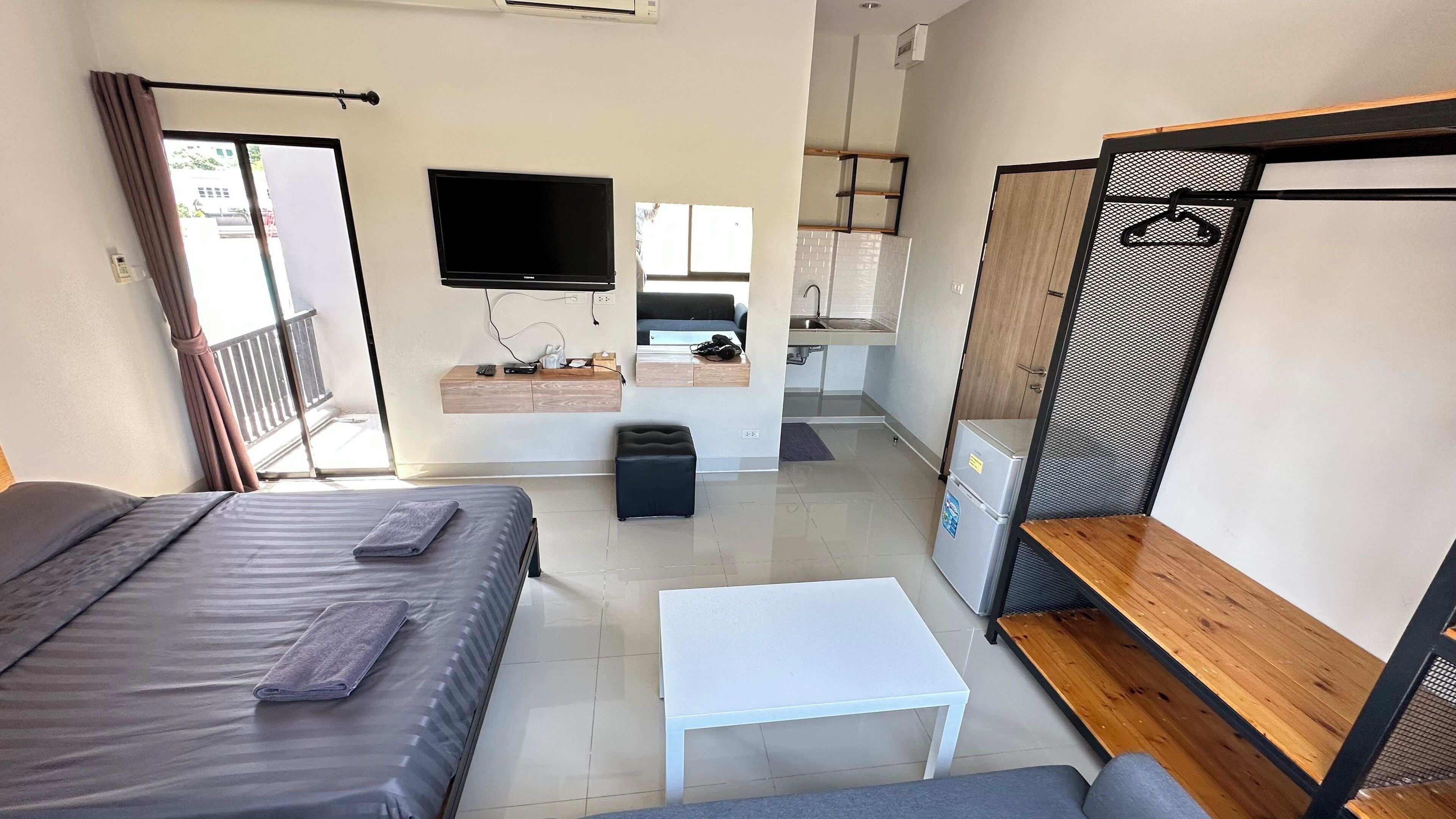 A compact hotel room with a bed, a small table, a kitchenette, and a TV.