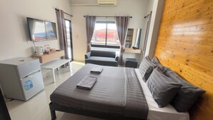 Una habitación de hotel con cama, escritorio, televisión y ventana con cortinas.