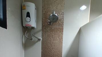 Un box de ducha estrecho con pared de azulejos, un cabezal de ducha manual y un calentador de agua instalado en la pared.