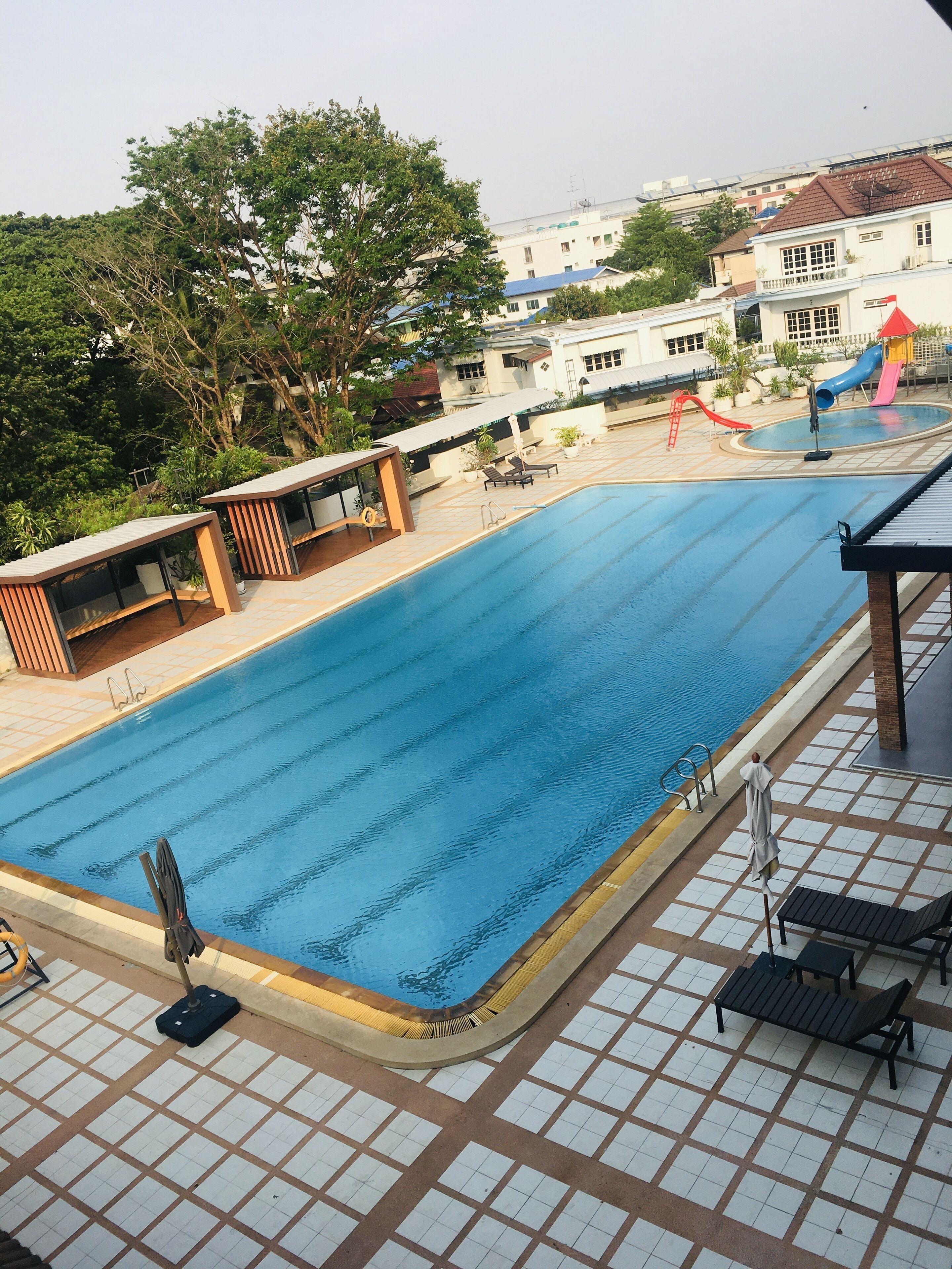 Una piscina con solárium de baldosas, sillas de descanso y una zona de juegos para niños con toboganes.