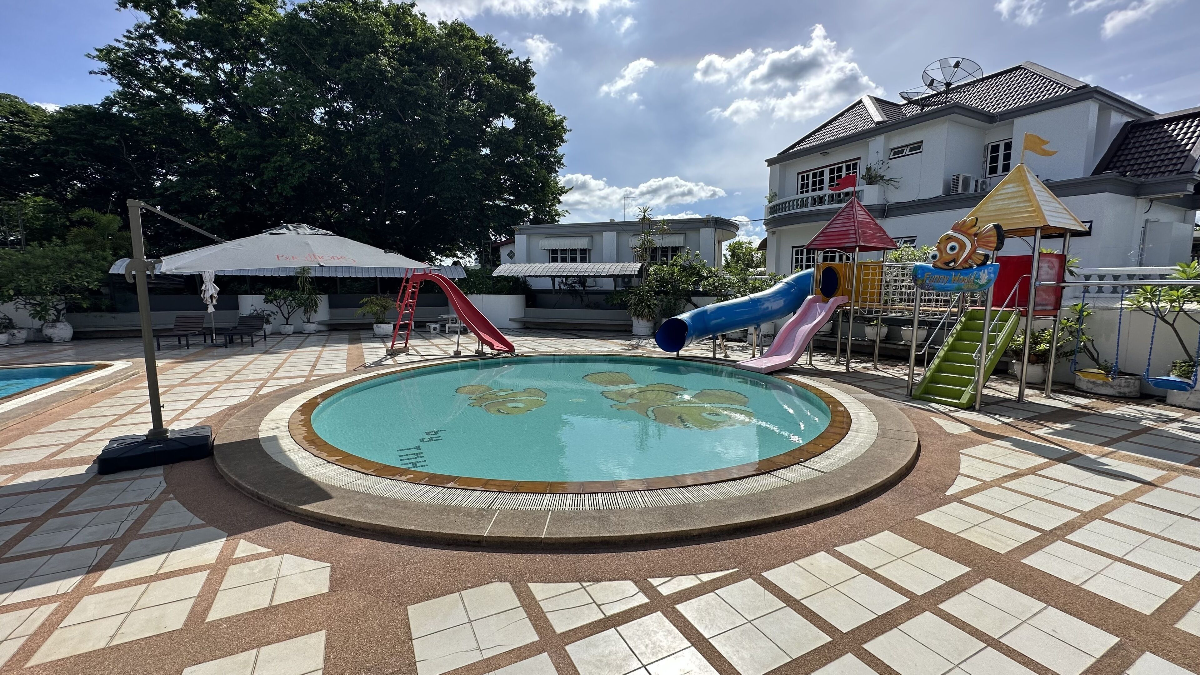 A swimming pool with a slide and a play structure, surrounded by a tiled patio.