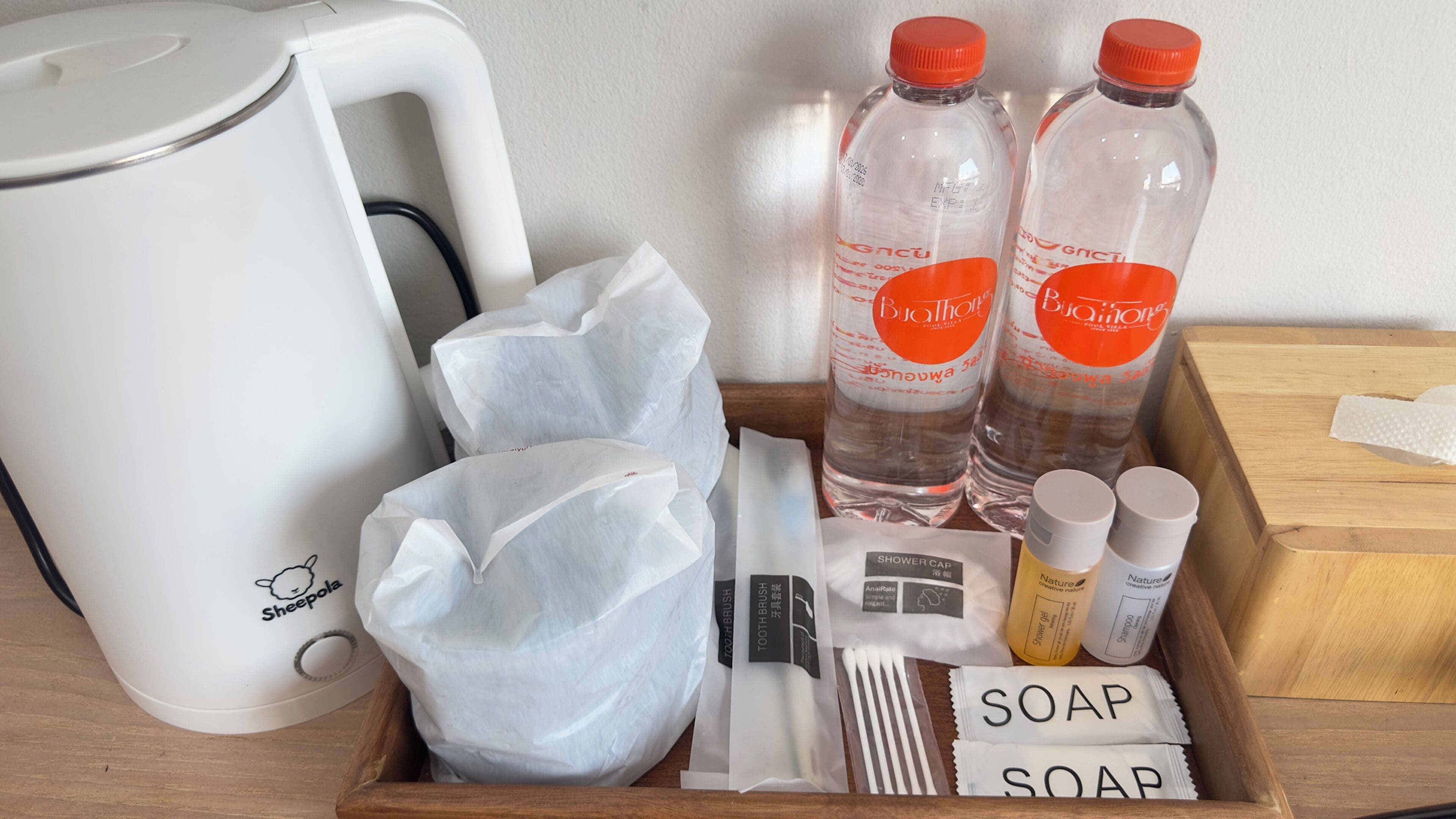 Bandeja de madera con artículos de aseo, incluyendo dos botellas de agua, un gorro de ducha, un cepillo de dientes, una pastilla de jabón y una botella de champú.