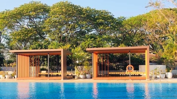 Una piscina con dos gazebos de madera, uno decorado con un símbolo de paz, rodeada de abundante vegetación.