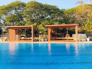 A swimming pool with two wooden gazebos, one with a peace sign decoration, surrounded by lush greenery.