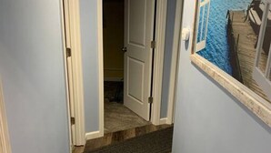 A narrow hallway with wooden flooring, a dark rug, and a door leading to another room. - Rye Beach Retreat · Cozy Cottage on Rye Beach with Lake Erie view! (Huron)