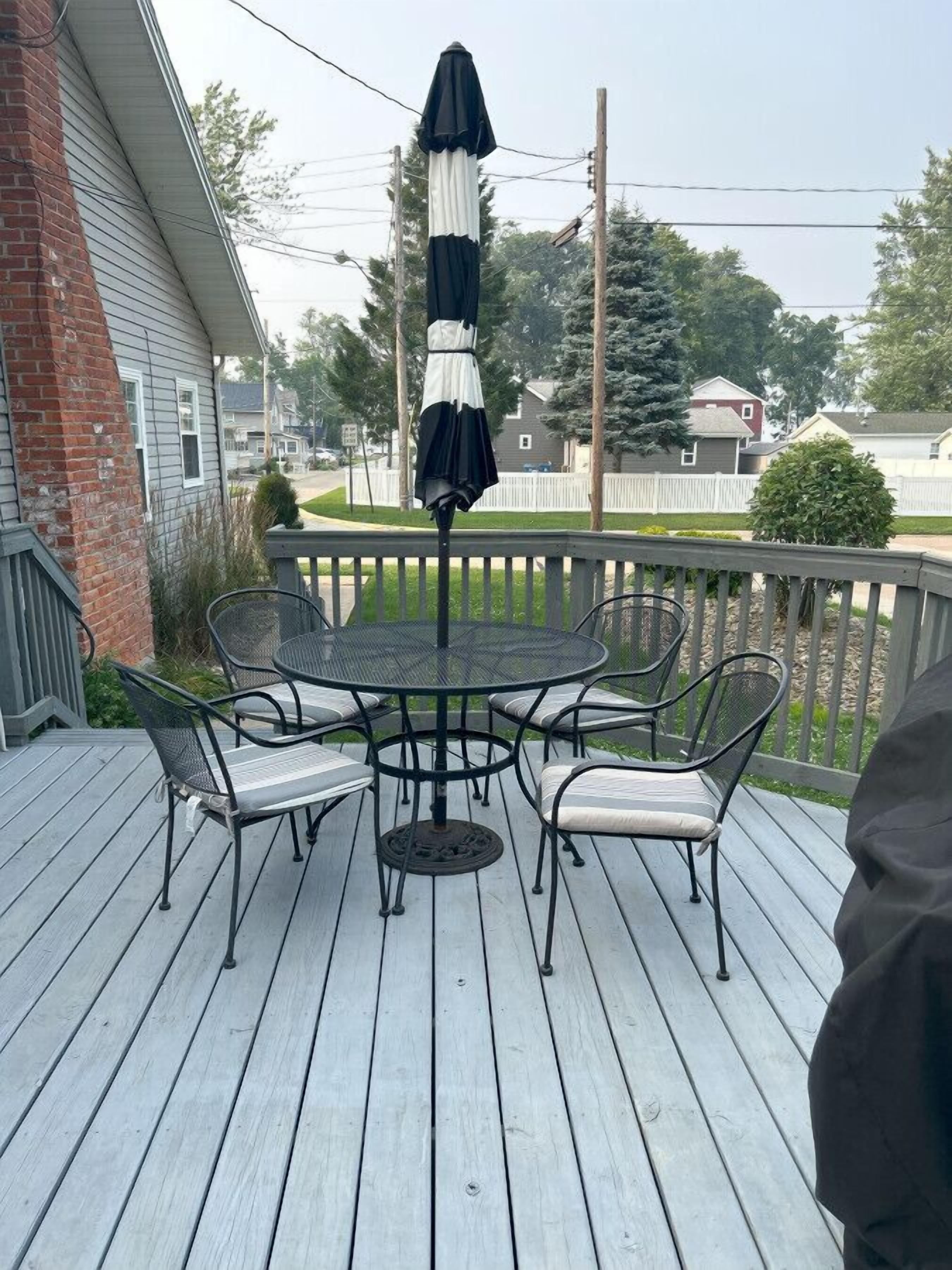 A wooden deck with a round table and chairs, an umbrella, and a brick wall.