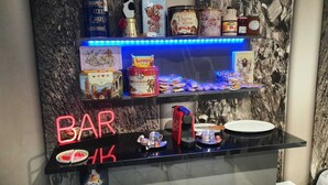 A bar area with a neon sign, shelves with various food items, and a coffee machine. - CMK Bar & Spa (Milton Keynes)