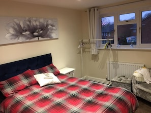 A bedroom with a bed, a nightstand, a radiator, and a window with curtains. - CMK Bar & Spa (Milton Keynes)
