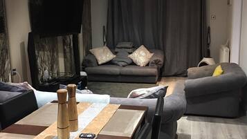 A modern living room with a sofa, a dining table with chairs, and a flat-screen TV mounted on the wall.