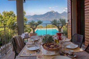 Un balcón con una mesa lista para comer, con vistas a una piscina y un paisaje montañoso.