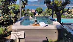 A hot tub with a bottle and glasses, surrounded by greenery and a sign that reads 'Welcome to SunnyHome Our Paradise For You.'