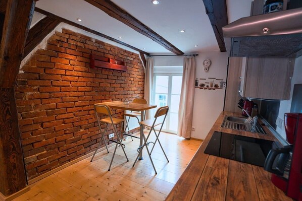 A kitchen with a brick wall, wooden floor, and a small dining table with chairs.