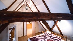A bedroom with a sloped ceiling, wooden beams, a bed with striped bedding, and a hanging light fixture. - RefuKium "Alte Gerberei" in der Innenstadt  (Weißenburg in Bayern)