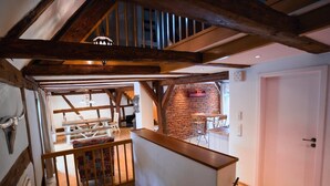 A loft-style room with exposed wooden beams, a brick wall, and a staircase leading to another level. - RefuKium "Alte Gerberei" in der Innenstadt  (Weißenburg in Bayern)