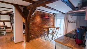 A kitchen with exposed wooden beams, a brick wall, and a wooden dining table with chairs. - RefuKium "Alte Gerberei" in der Innenstadt  (Weißenburg in Bayern)