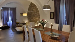 A dining area with a wooden table, white chairs, a stone wall, and a modern pendant light. - VILLA FENICE (Sicilia)
