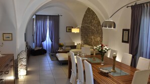 A dining area with a wooden table, white chairs, and a stone wall. - VILLA FENICE (Sicilia)