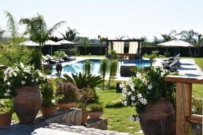 A pool area with lounge chairs and umbrellas, surrounded by potted plants and a grassy lawn. - VILLA FENICE (Sicilia)