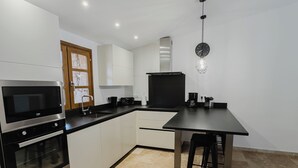 Une cuisine moderne avec des meubles blancs, un four encastré, un four à micro-ondes et un coin repas comprenant une table et des chaises.