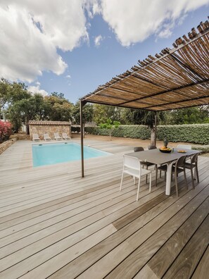 Un patio in legno con piscina, area relax all'aperto e un pergolato.