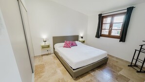 Une chambre à coucher avec un lit, des tables de chevet, une fenêtre avec des rideaux et une petite table.