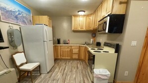 Una cocina compacta con armarios de madera, un refrigerador blanco, un microondas, una estufa y una silla.