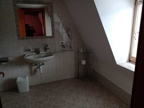 Een kleine, eenvoudige badkamer met een wastafel, spiegel en raam.