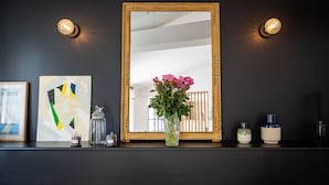 A dark wall with a large mirror, a vase with pink flowers, and two framed artworks. - La Mignonne - Village house with swimming pool (Saint-Didier-au-Mont-d'Or)
