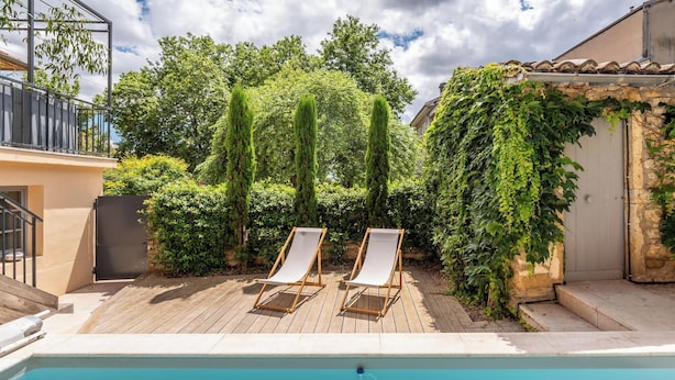 A pool area with two lounge chairs, a wooden deck, and a stone wall with ivy. - La Mignonne - Village house with swimming pool (Saint-Didier-au-Mont-d'Or)