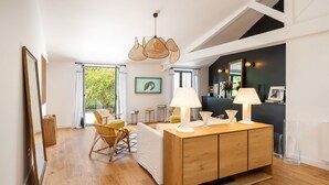 A modern living room with a wooden cabinet, two lamps, a large mirror, and a view of greenery outside. - La Mignonne - Village house with swimming pool (Saint-Didier-au-Mont-d'Or)