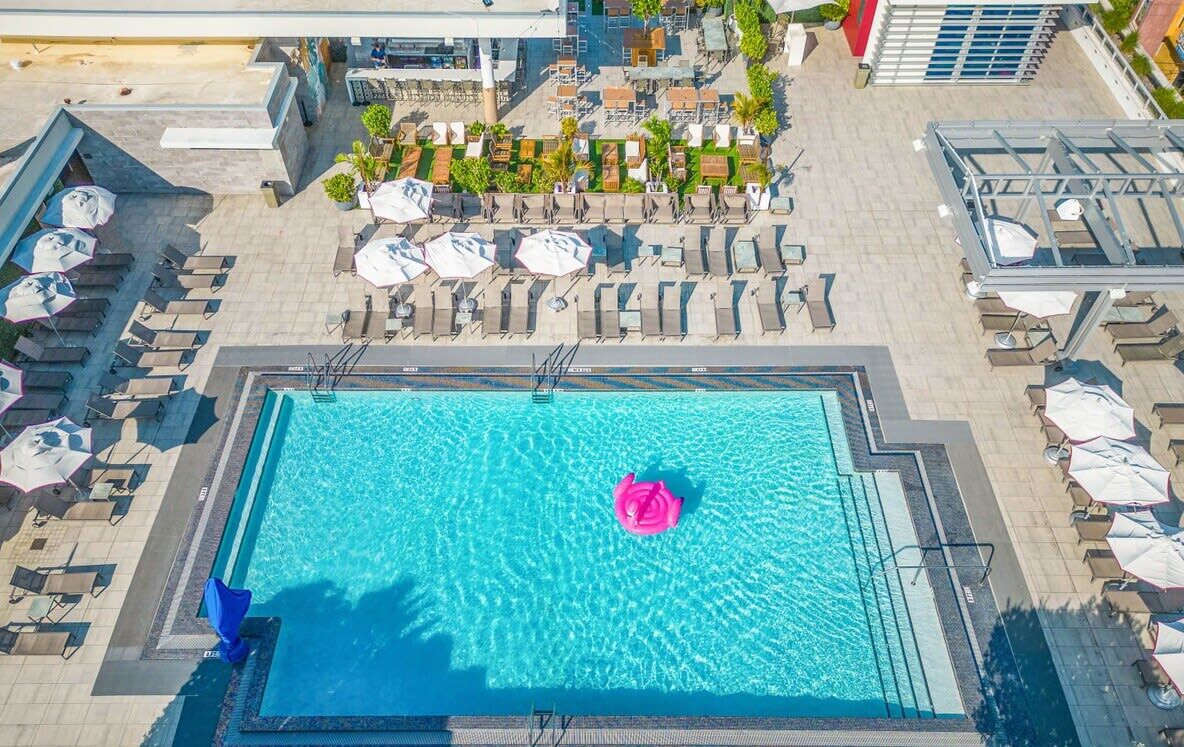 An aerial view of a swimming pool with lounge chairs and umbrellas, surrounded by buildings.
