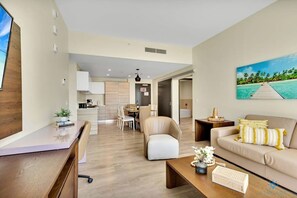 A modern living room with a sofa, coffee table, and a TV. There is a dining area with chairs and a table in the background. - Condo Resort + Front Bay View & Rooftop Pool (Hollywood)