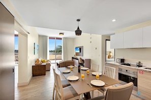 A modern dining area with a table set for four, a kitchen with white cabinets, and a large window offering a view.