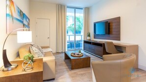 Una sala de estar moderna con un sofá, una mesa de centro y un televisor. Hay un balcón con vistas a palmeras.
