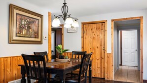 Un coin repas avec une table en bois, quatre chaises, un lustre et un tableau encadré au mur.
