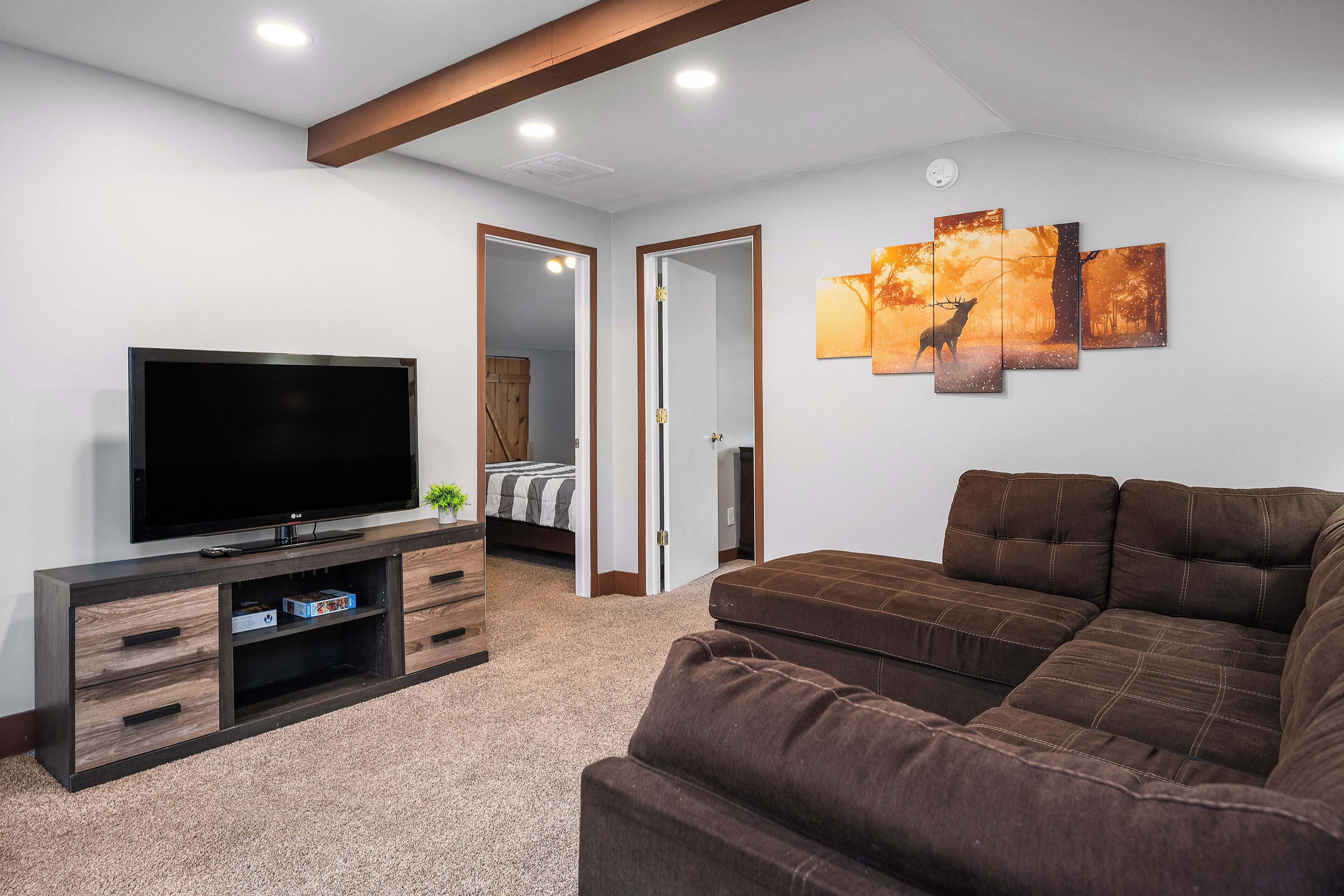 A modern living room with a flat-screen TV, a brown sectional sofa, and a multi-panel artwork on the wall.