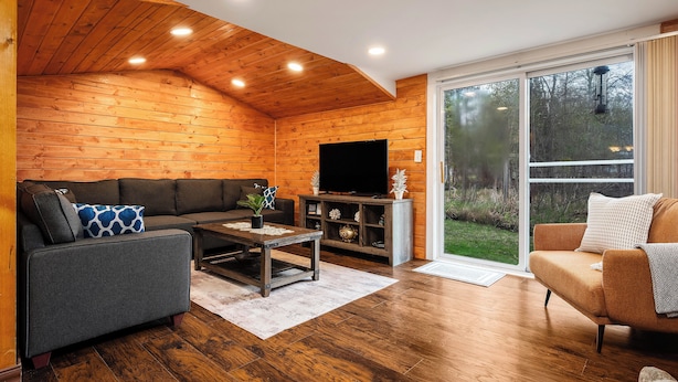 Un salon chaleureux avec un plafond en bois, un téléviseur à écran plat, un canapé gris, un canapé marron et une table basse.