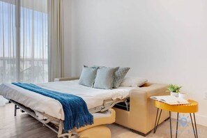 A modern bedroom with a bed, a small side table, and a view through large windows.