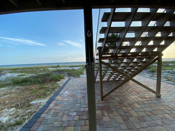 A view through a wooden pergola with a brick pathway leading to a beach.