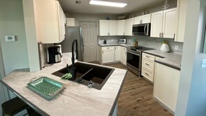 A modern kitchen with white cabinets, a stainless steel sink, a microwave, and a stove. - Your Dream Getaway - A Slice of Heaven (St Joe Beach)