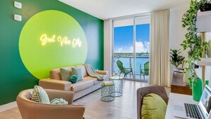 A modern living room with a green accent wall, a sofa, a coffee table, and a laptop on a desk. - Sunset Relaxation |Modern Apartment| Pool| Gym (Hollywood)