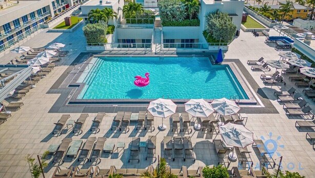 A resort with a swimming pool, sun loungers, and a view of the ocean at sunset. - Sunset Relaxation |Modern Apartment| Pool| Gym (Hollywood)
