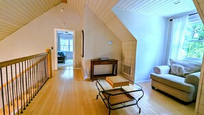 A spacious loft with a high ceiling, a wooden staircase, a seating area with a sofa, and a small table. - Pet-Friendly Suite in North Georgia Mountains with Kitchen, Dining & Living Room (Dahlonega)